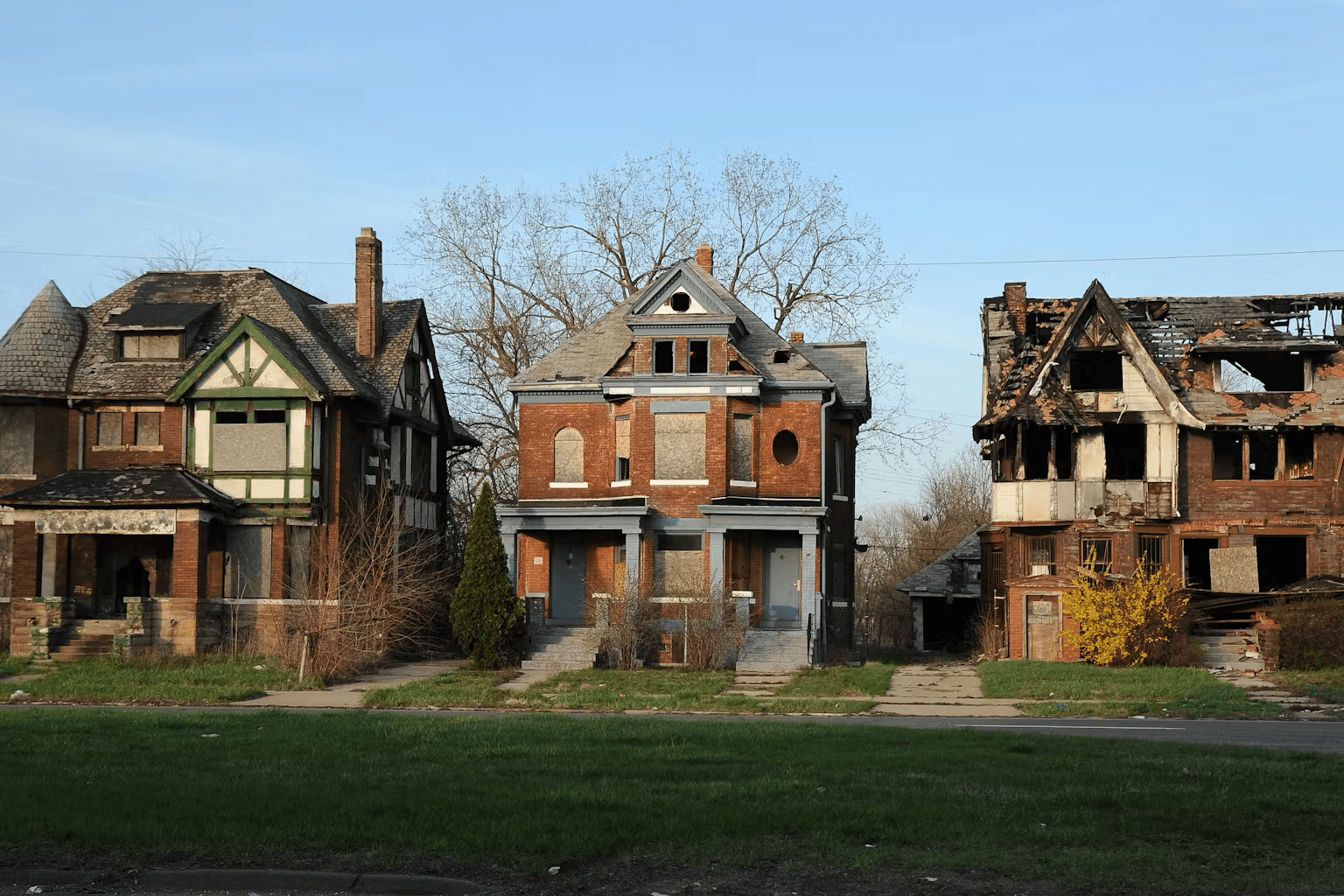 A block of three abandoned houses, boarded up and fire damaged, on an empty street