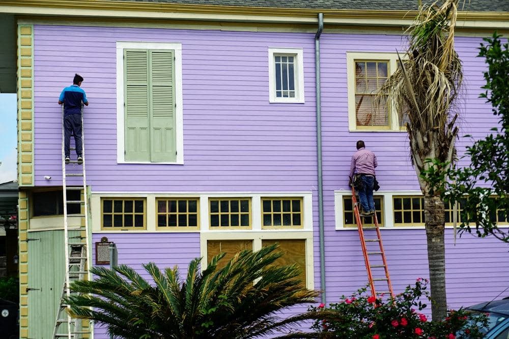 Tradespeople on ladders repainting the exterior of a house