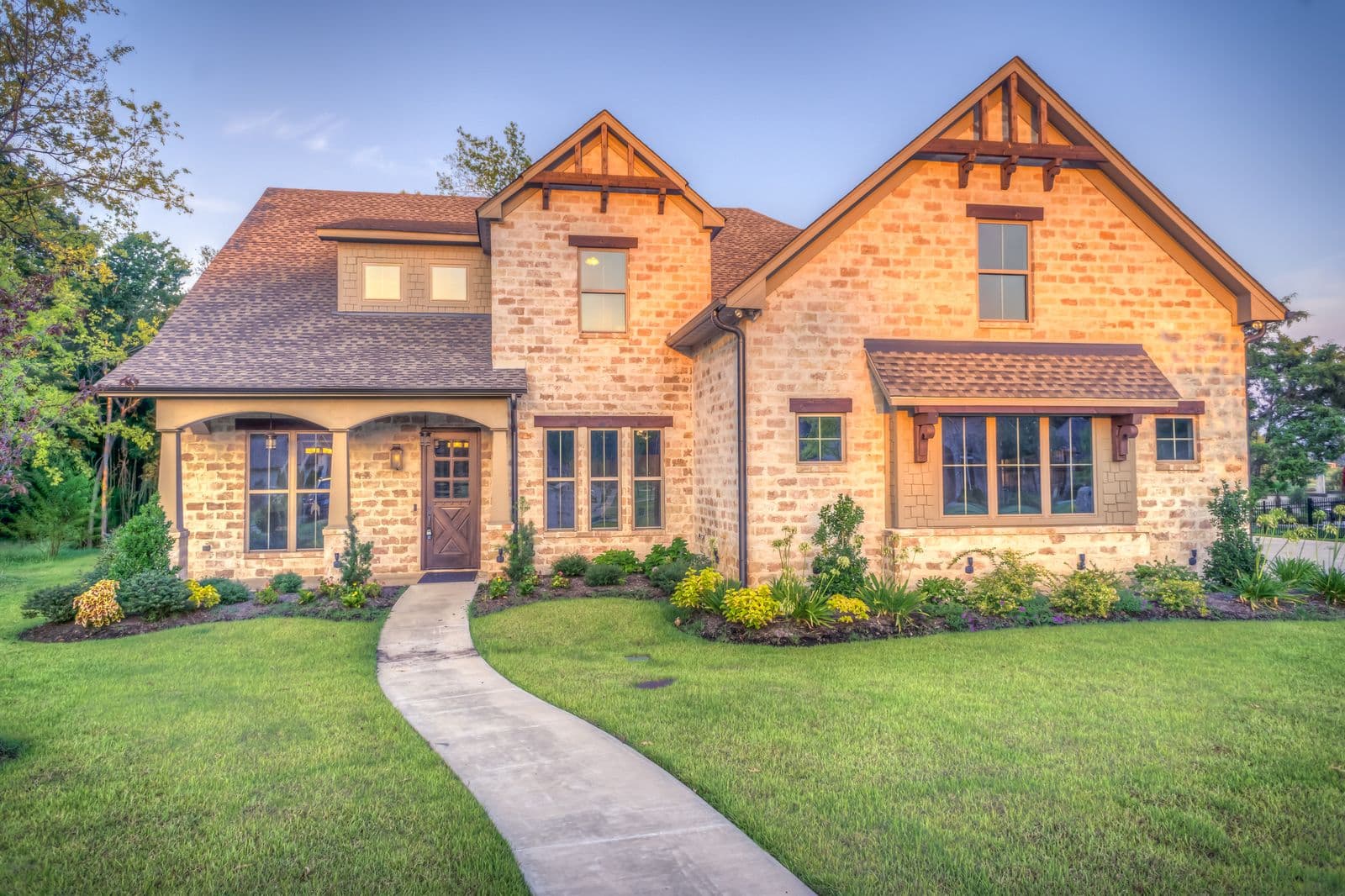A warm brick family home at dusk with its porch lights on