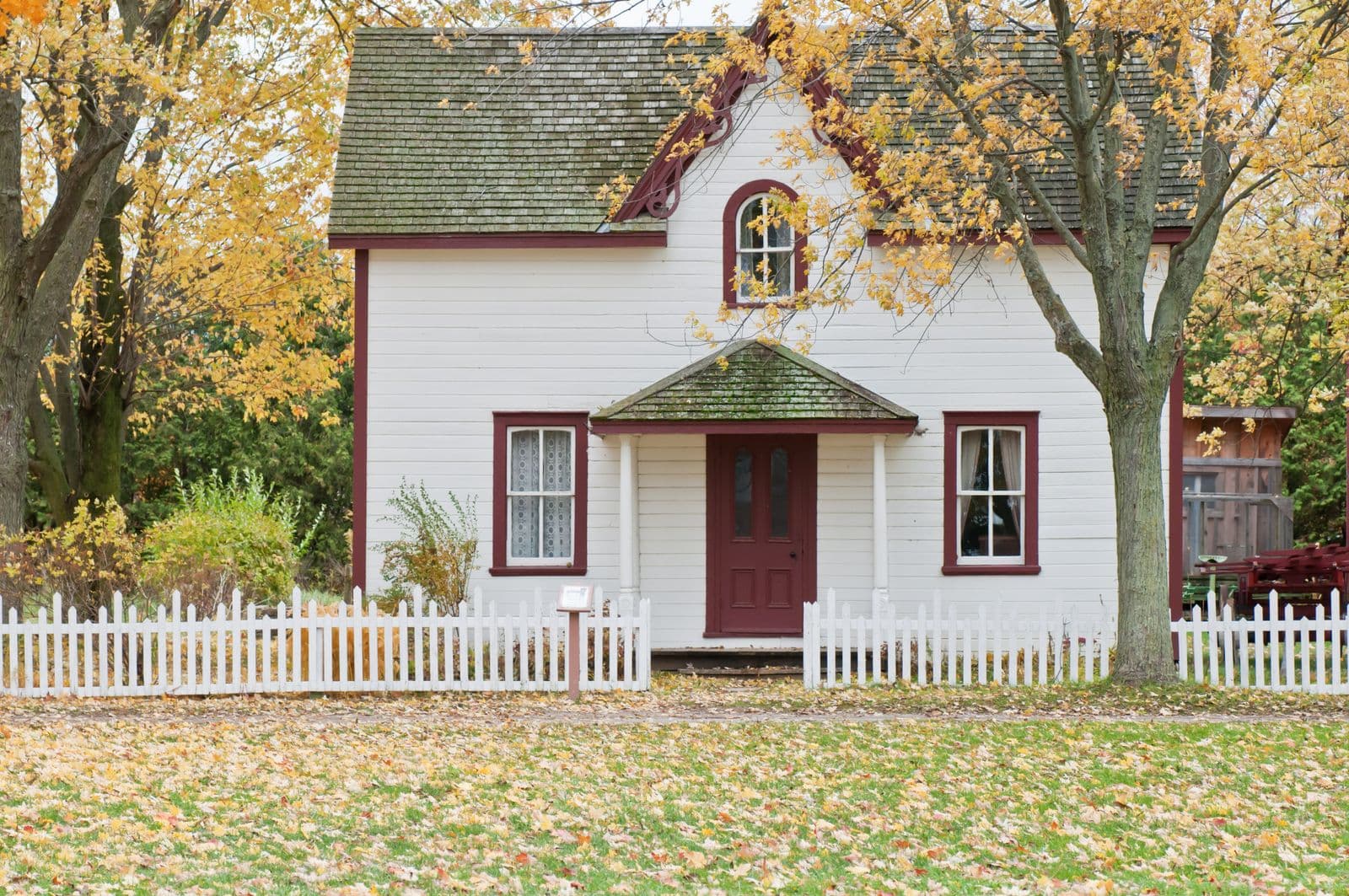 An older detached home behind a white picket fence